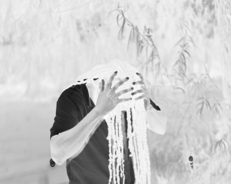Inverted portrait of a person covering their face with strands or fabric